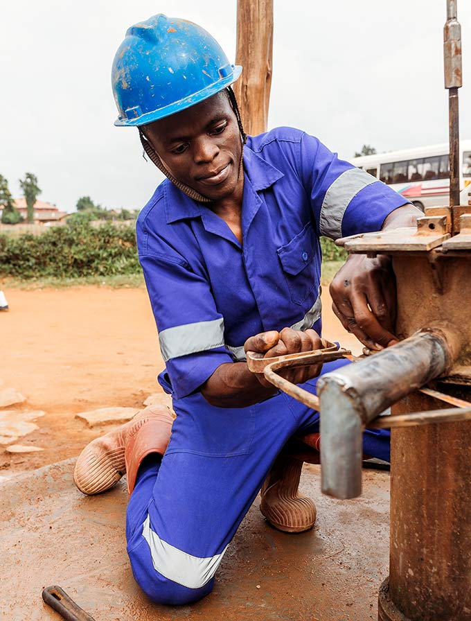 A Ugandan technician sawing into the side of a borehole well during a repair